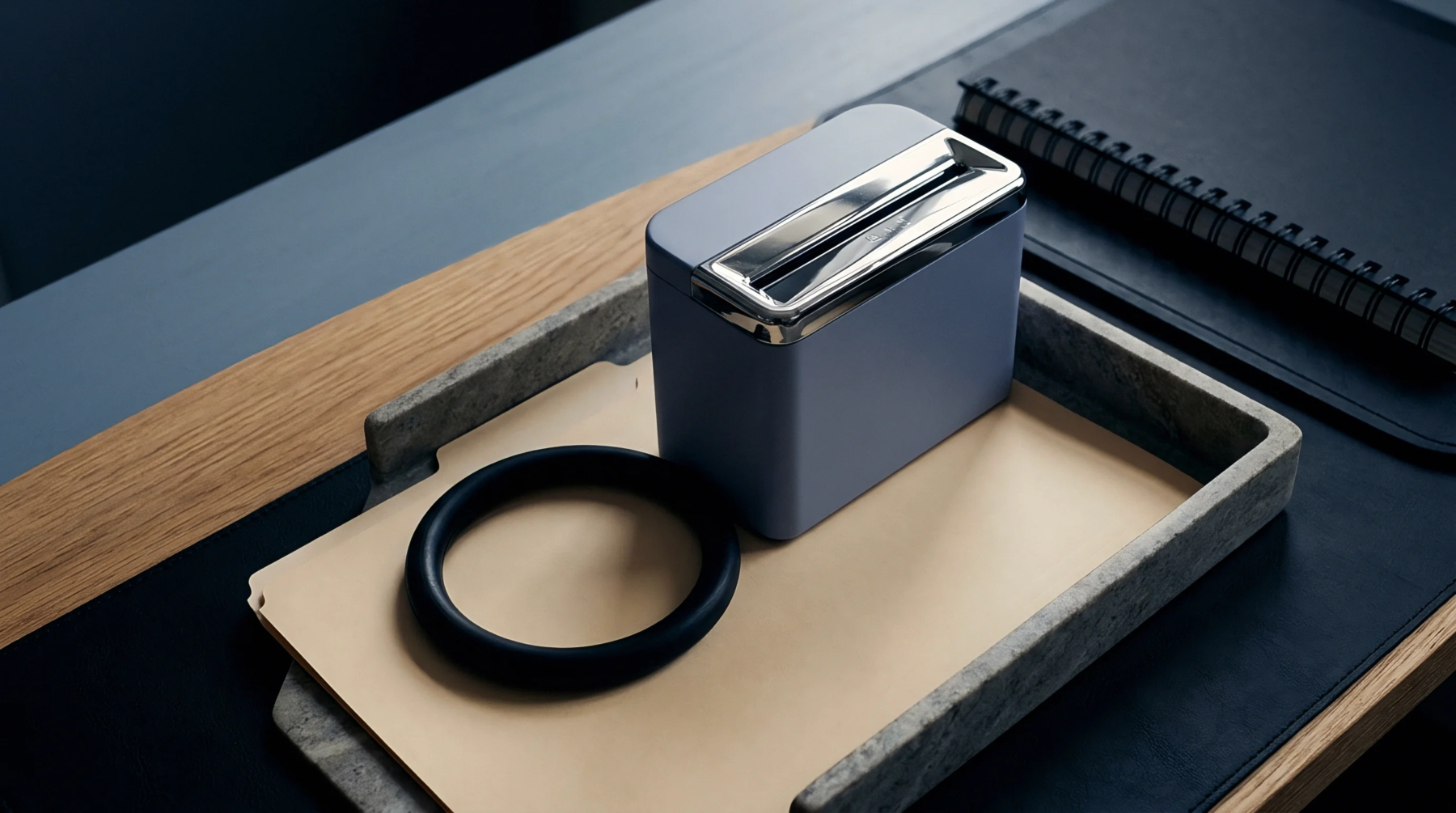 A compact processing unit and circular component are arranged on a tray within a structured workspace with paper and a bound notebook.