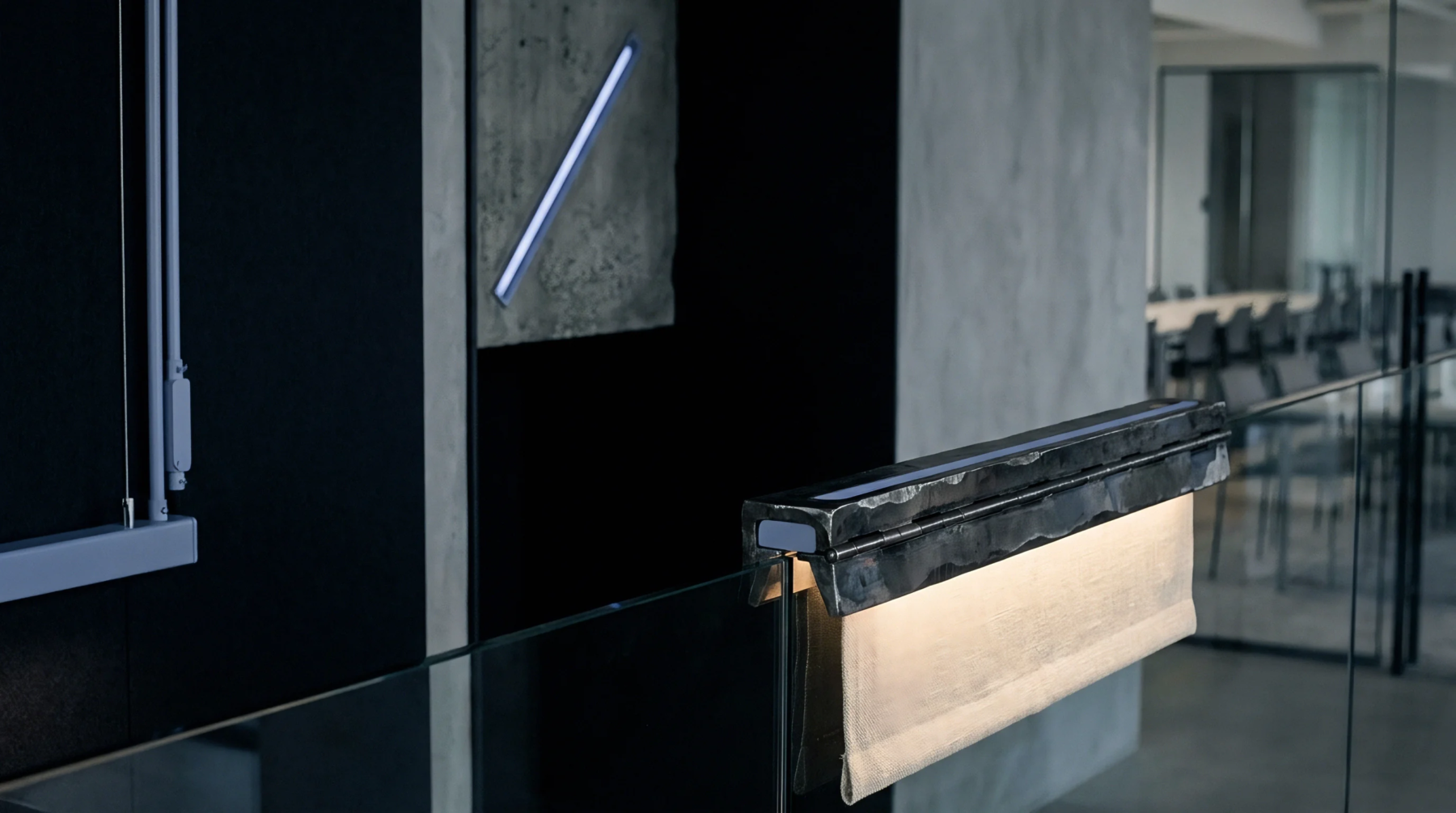 Textile and hammered metal light fixture rests on a glass balustrade inside a modern industrial corporate office environment.