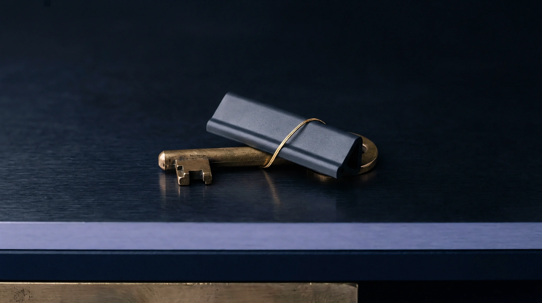 A dark matte polymer industrial component is securely bound with fine wire to a cast brass skeleton key resting on a dark work surface.