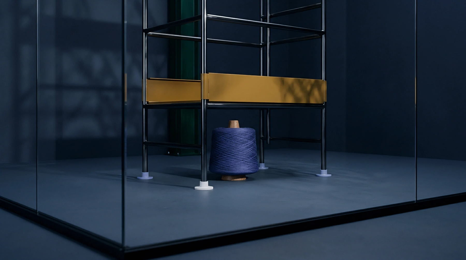 Polished steel supports with yellow structural plating stand over a large spool of dark blue industrial textile yarn inside a glass enclosure.