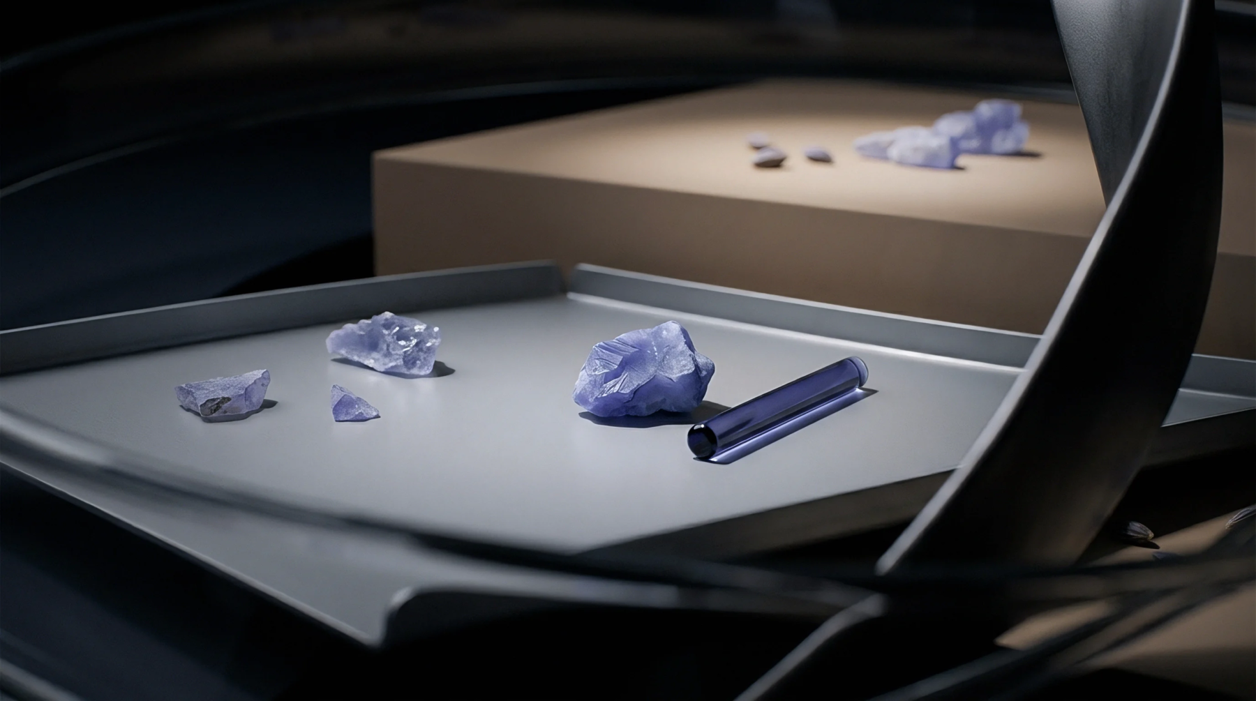 Raw violet mineral samples and a cylindrical specimen rest upon a metallic tray alongside a processed beige platform containing additional raw inventory.