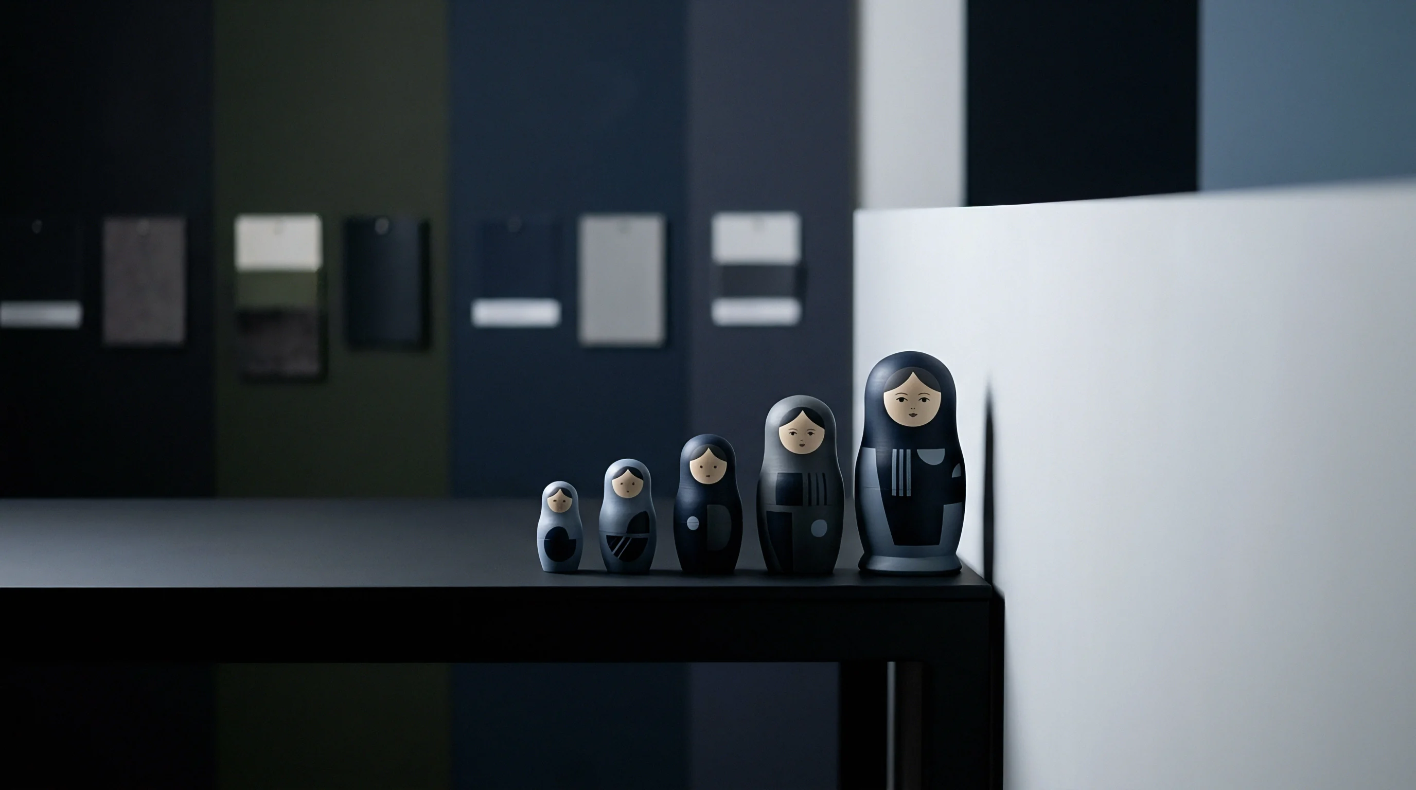 Five turned wooden artifacts of graduated sizing stand aligned on a dark workbench inside an industrial design studio.
