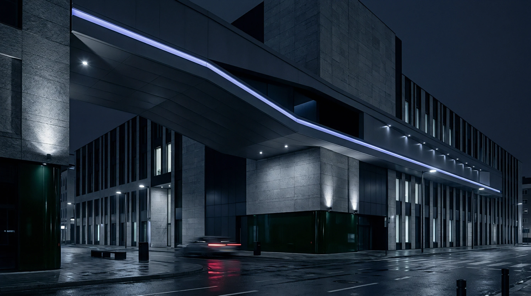 Dark granite and glass facade elements define the wet urban street corridor outside this corporate facility at night.